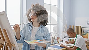 Young man and beautiful woman artists immersed in a serious drawing lesson together, standing in a relaxed art studio wielding