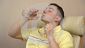 The young man became hot and he drinks water from a bottle closeup. A man waves his hands because the room is stuffy.