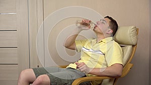 The young man became hot and he drinks water from a bottle. A man waves his hands because the room is stuffy.