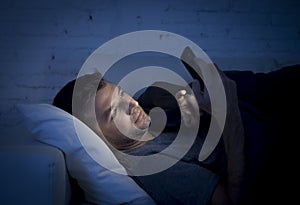 Young man in bed couch at home late at night texting on mobile phone in low light relaxed