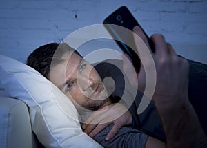 Young man in bed couch at home late at night using mobile phone in low light relaxed in communication technology concept