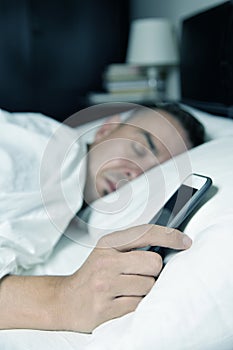 Young man in bed grabbing his smartphone