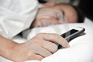 Young man in bed grabbing his smartphone