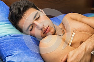 Young man in bed measuring fever with thermometer