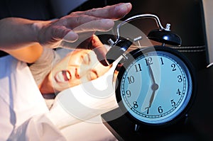 Young man in bed stopping the alarm clock