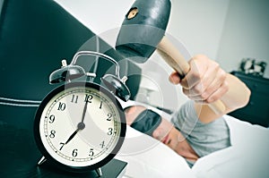 Young man in bed about to hammer his alarm clock