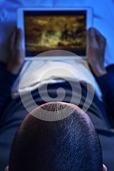 Young man in bed watching a movie or a series in his tablet