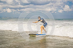 Young man, beginner Surfer learns to surf on a sea foam on the Bali island