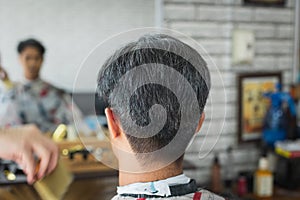Young man being haircut with scissor by professional barber in barbershop. Hairdresser using comb and scissors cut hair