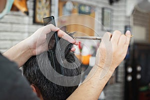 Young man being haircut with scissor by professional barber in barbershop. Hairdresser using comb and scissors cut hair