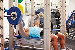 Young man bench pressing weights at a gym, side view