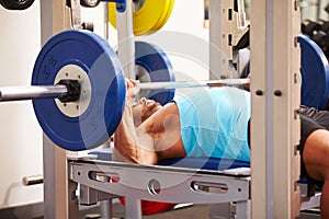 Young man bench pressing weights at a gym, side view