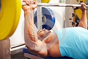 Young man bench pressing weights at a gym, side view close-up