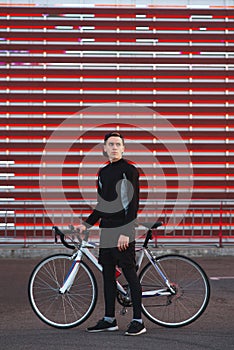 A young man with a bicycle and athletic dress is on an abstract red background