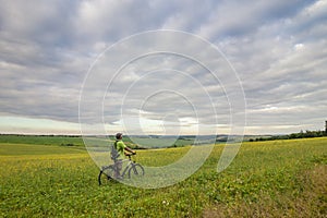 Young man with a bicycle on green field on a sunny summer day