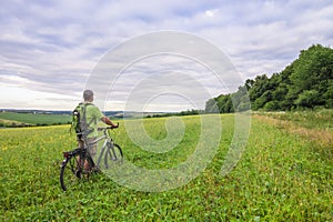 Young man with a bicycle on green field on a sunny summer day
