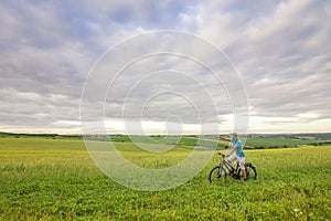 Young man with a bicycle on green field on a sunny summer day