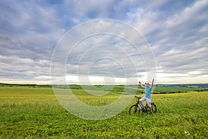 Young man with a bicycle on green field on a sunny summer day