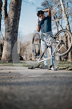 Young man with bicycle making a call in the park on a sunny day