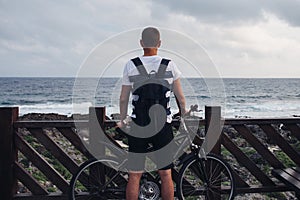 Young man with bicycle standing by the shore looking at the sea and the sky.