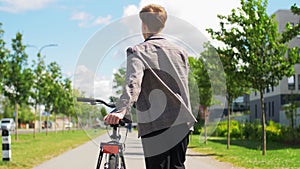 Young man with bicycle walking along city street