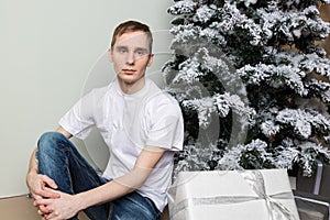 Young man with big present sitting on floor near christmas tree