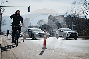 Young man biking in the city while talking on the phone with traffic around