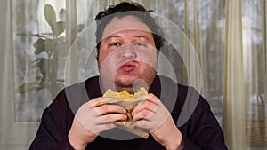 Young man bites sandwich. Fat guy eats fast food. Very hungry guy.