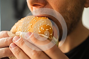 Young man biting fresh tasty hamburger close-up