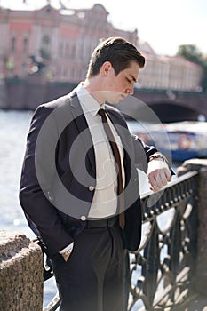 A young man in a black business suit, white shirt and tie looks at the clock