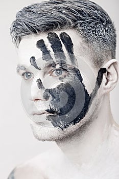 Young man with black hand print on white face. Closeup Portrait. Professional Fashion Makeup. fantasy art makeup