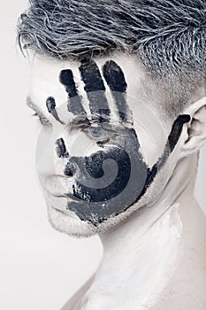 Young man with black hand print on white face. Closeup Portrait. Professional Fashion Makeup. fantasy art makeup