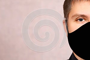 A young man in a black mask on a light background. necessary protection from covid-19. fabric reusable mask the guy does not have