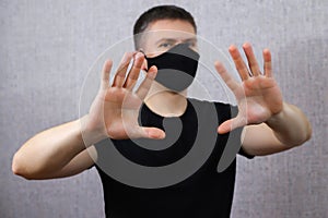 Young man in a black medical mask shows his hands STOP. Guy on a light background. Fear of a coronavirus infection. Covid-19