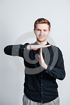 Young man in a black shirt shows a time out sign with his hands on a white background. Copy, empty space for text