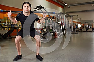 Young man in the black sportwear with bar flexing muscles in gym. sport, fitness, bodybuilding