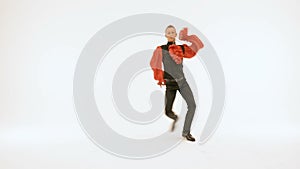 A young man in a black suit and a red shirt beautifully dances on a white background.
