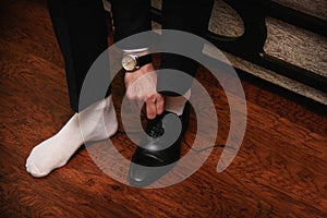 Young man in a black suit and white socks wears his black shoes on a dark background