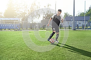 A young man in a black uniform with the number 21 is playing football on the soccer field of the stadium alone