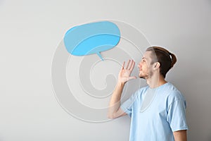 Young man and blank speech bubble on light background