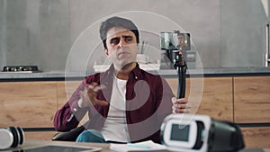 Young man blogger recording video blog using his mobile phone on tripod in the kitchen of his home.