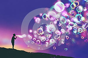 Young man blowing glowing soap bubbles against evening sky