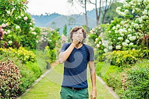 Young man blowing nose in front of blooming tree. Spring allergy concept