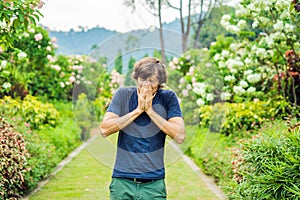 Young man blowing nose in front of blooming tree. Spring allergy concept