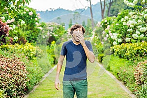 Young man blowing nose in front of blooming tree. Spring allergy concept