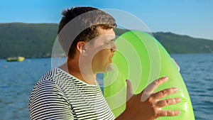 Young man blowing up an inflatable swimming ring for his kids on a beach at sunset, emphasizing the concept of tourism