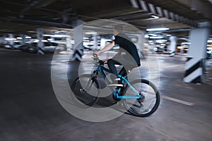 Young man on a blue bike rides through an underground parking lot. Cyclist can ride in an underground parking lot