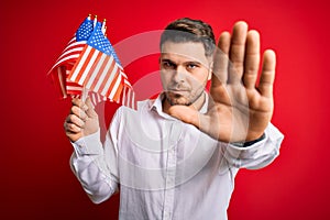 Young man with blue eyes holding flag of united states of america over red isolated background with open hand doing stop sign with