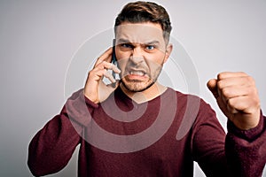 Young man with blue eyes speaking on the phone having a conversation on smartphone annoyed and frustrated shouting with anger,