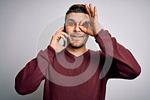 Young man with blue eyes speaking on the phone having a conversation on smartphone with happy face smiling doing ok sign with hand